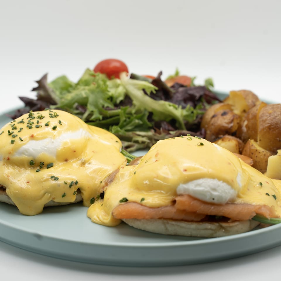 Eggs Benedict with smoked salmon, hollandaise sauce, chives, roasted potatoes, and a side salad.