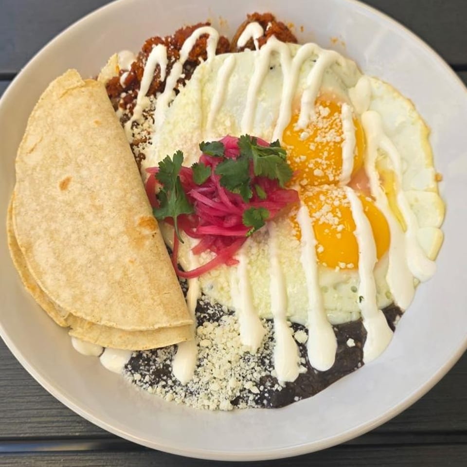 A white plate of chilaquiles with fried eggs, black beans, tortillas, and pickled onions.