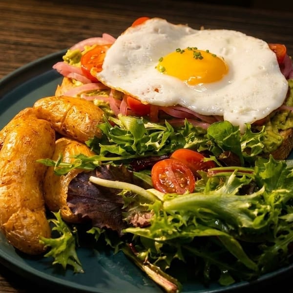Avocado toast with a fried egg, roasted potatoes, and a side salad on a dark plate.