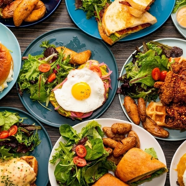Overhead view of a table laden with various brunch dishes, including sandwiches, waffles, and salads.