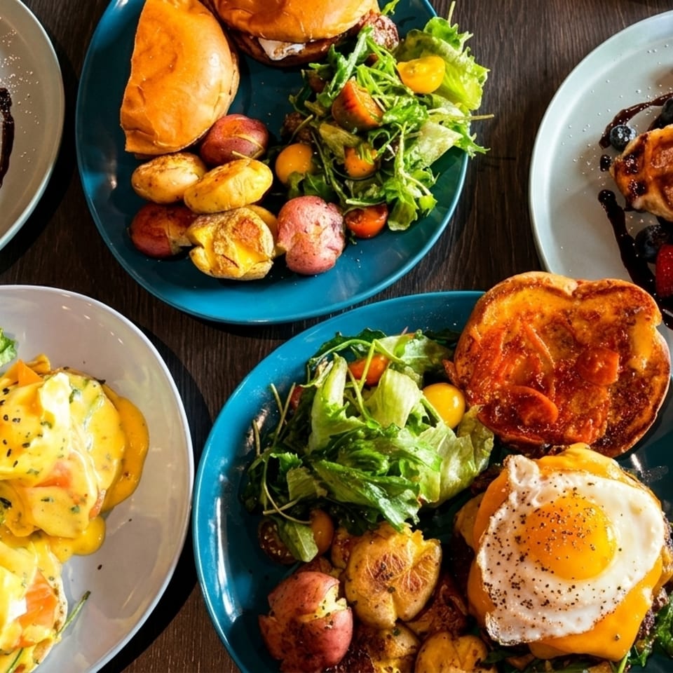 Overhead view of a table laden with various breakfast and brunch dishes, including waffles, eggs benedict, and burgers.