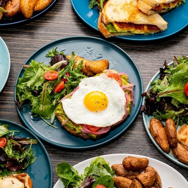 Assortment of brunch dishes including sandwiches, avocado toast with egg, and chicken and waffles.
